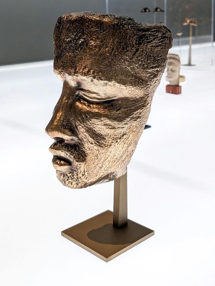 Bronze face on a brass stand, shown in a display case