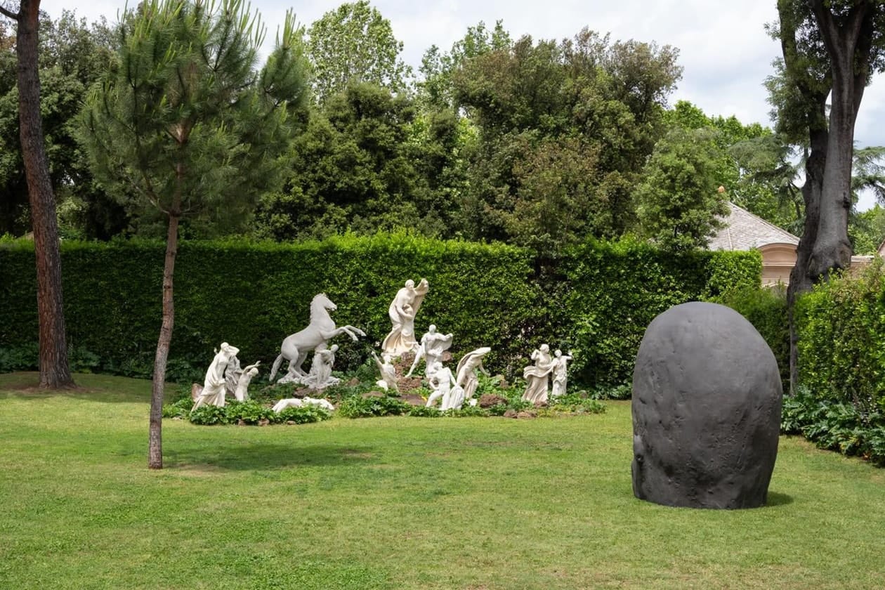 Monumental dark bronze head on the lawn of the Villa Medici gardens, antique group and umbrella pines