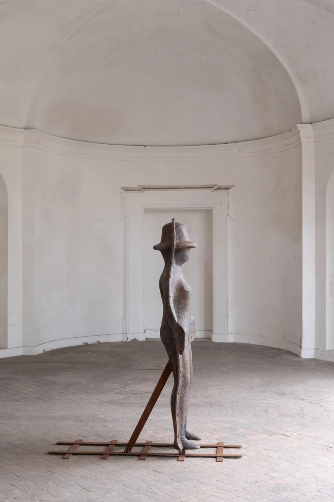 Standing hatted figure set on rails, in a white vaulted room