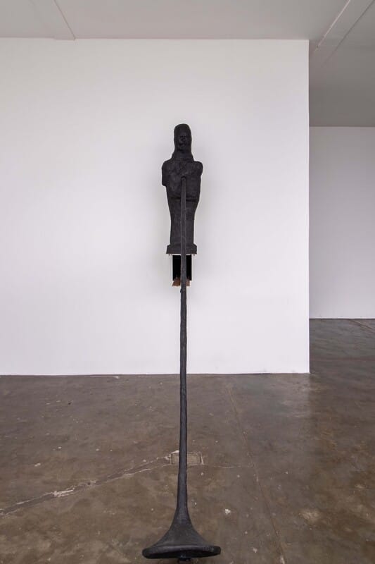 Hatted figure perched on a bronze stem flaring at its base